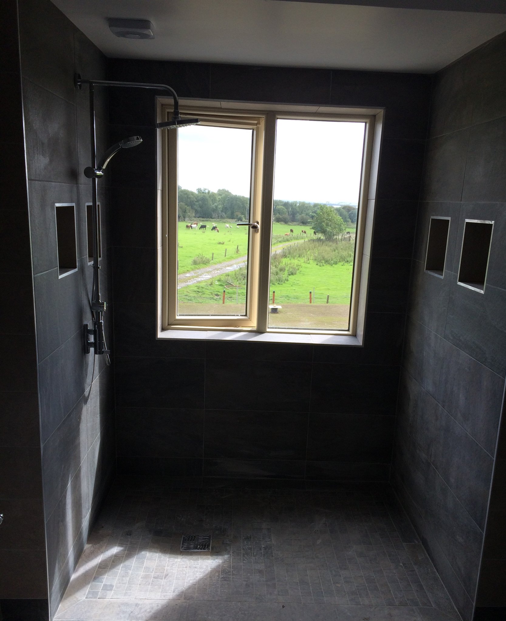 Level-access wet room shower with dark tiles and a window onto fields